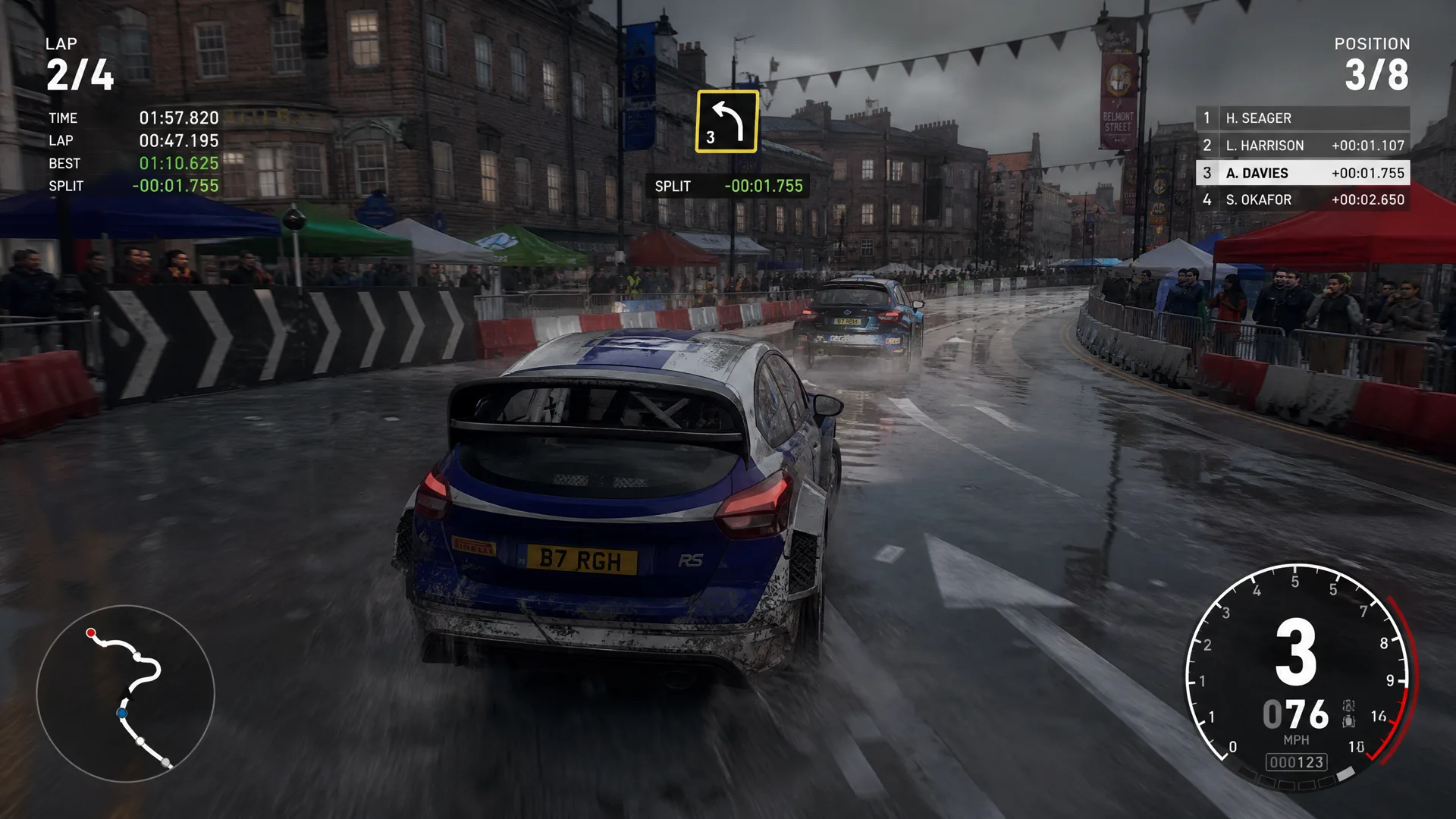 A rally car sliding through a wet British city-centre stage.